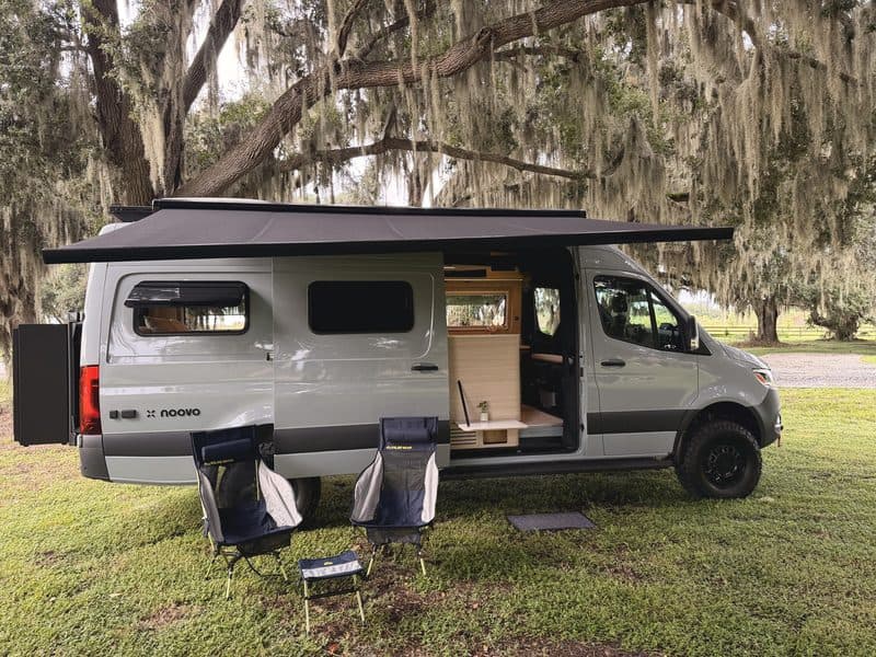 Nellie with the awning out, two camp chairs and a small table on the grass