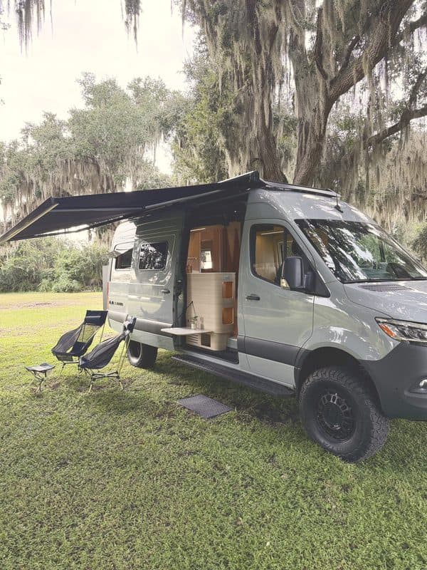 Nellie with the awning out and camp chairs under live oaks