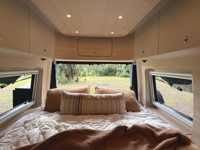 The bed with pillows, rear windows looking out to palms