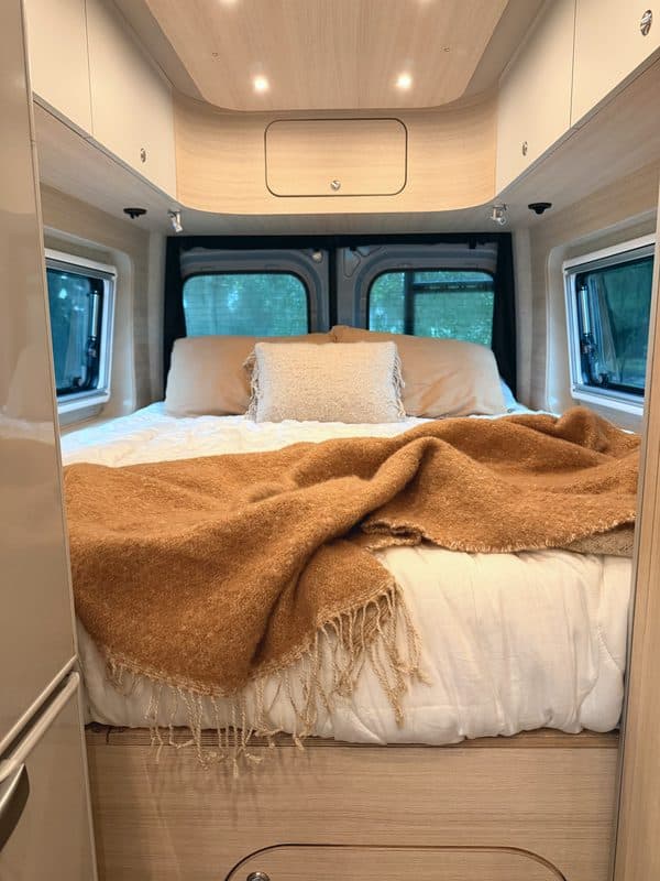 The bed with a caramel throw and the rear windows