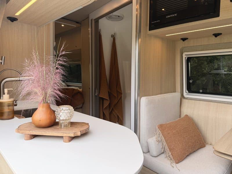 The dinette table with a vase of pink muhly, towels hanging by the shower