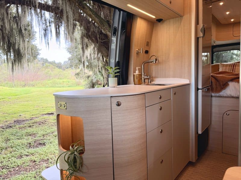 The curved galley cabinet and sink, with live oaks outside the open door