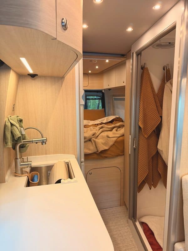 The galley sink and the shower with towels hanging, bed beyond
