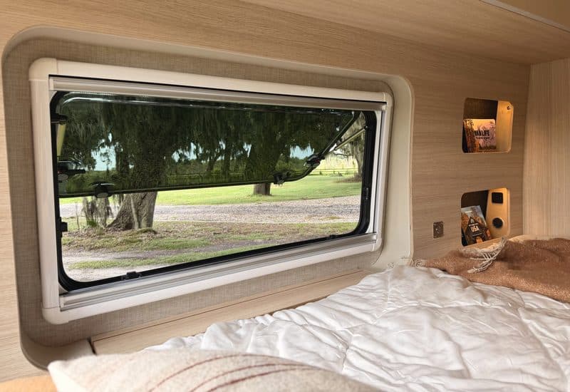The side window by the bed, looking out to oaks and a gravel drive