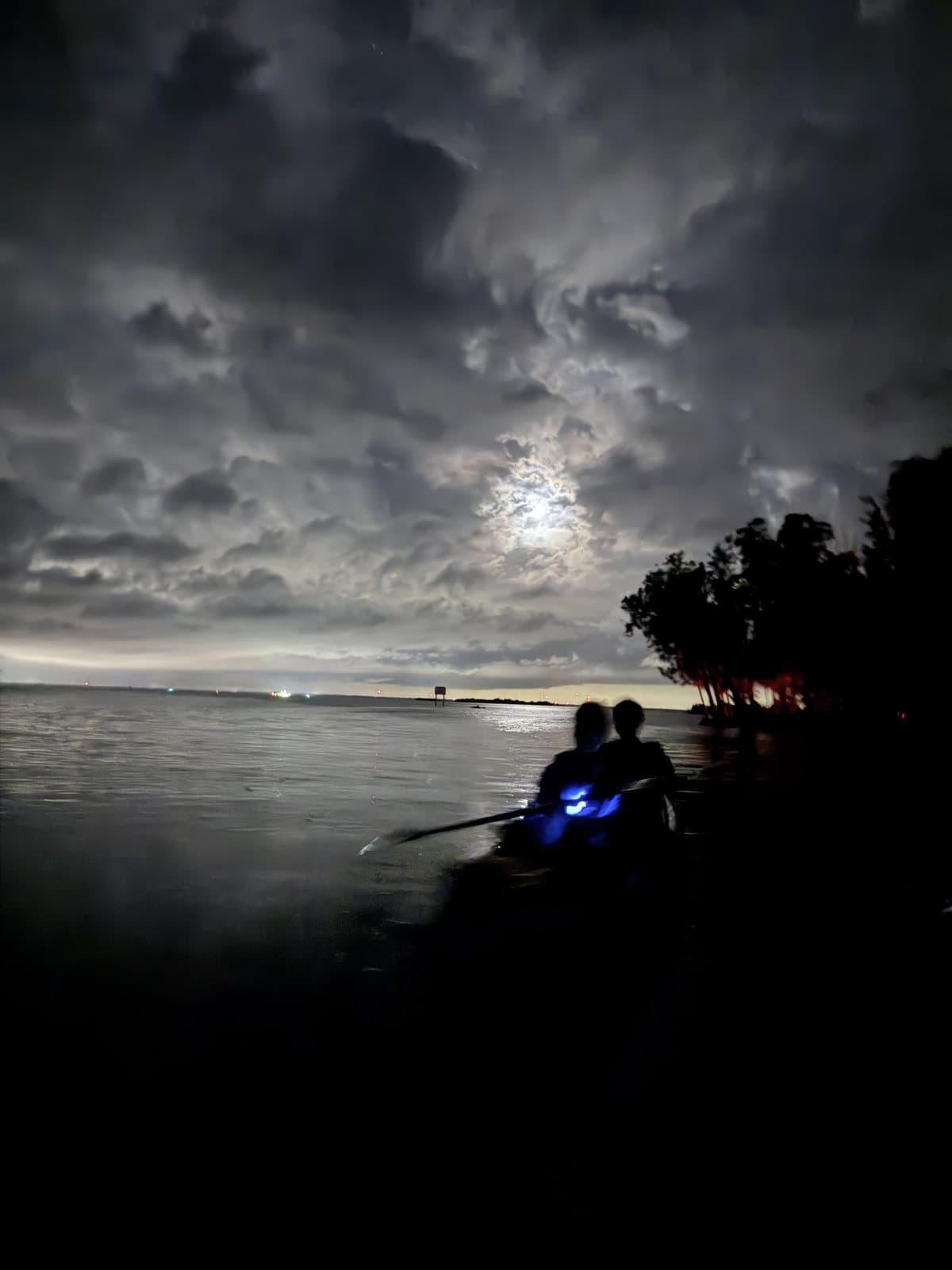 Bioluminescent kayaking near Titusville under a cloudy moon, with blue glow at the paddle