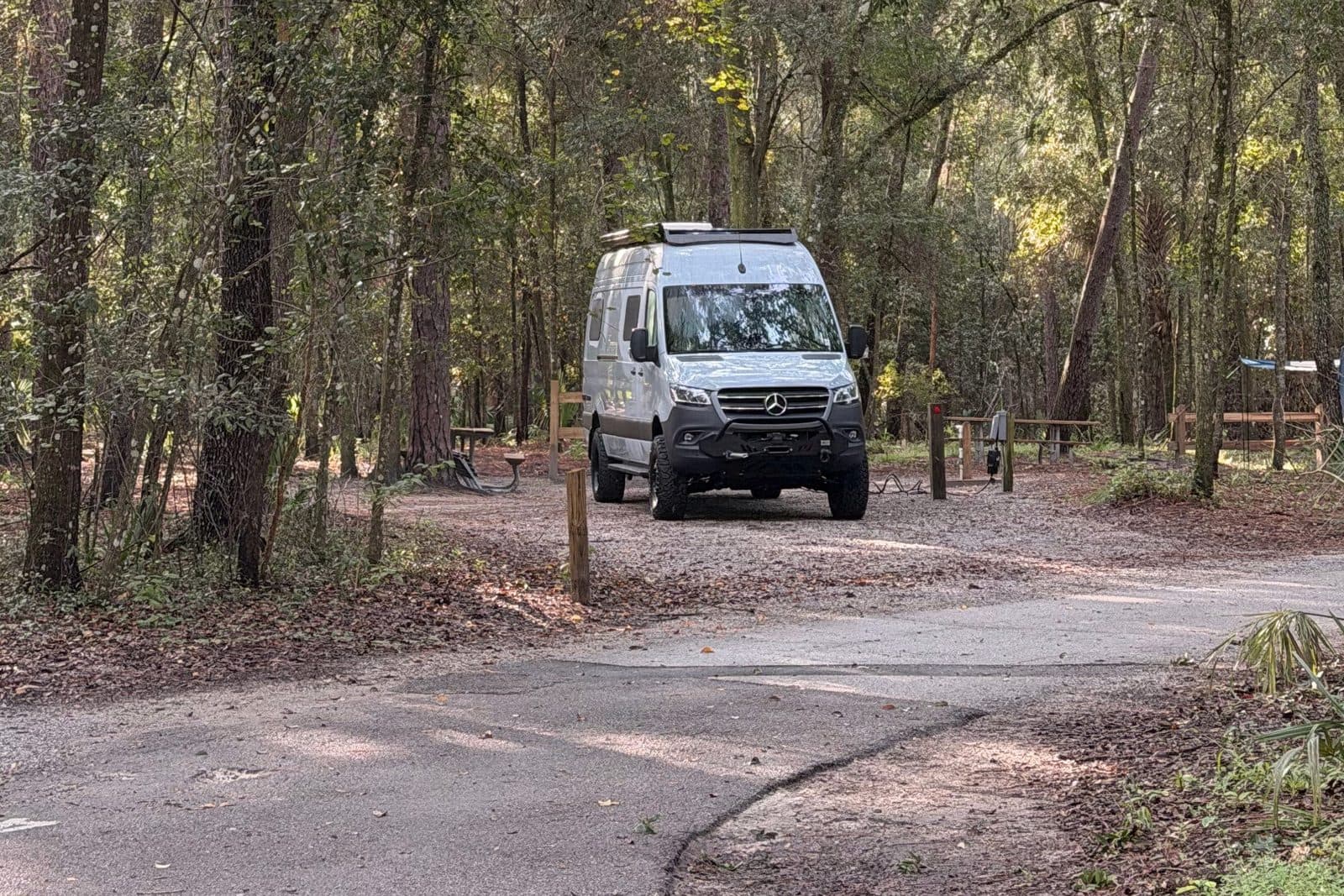 Nellie, a blue-gray Mercedes Sprinter camper van, parked at campsite 44 under tall oaks at Wekiwa Springs State Park in Apopka, Florida, with the paved camp loop road curving past in the foreground